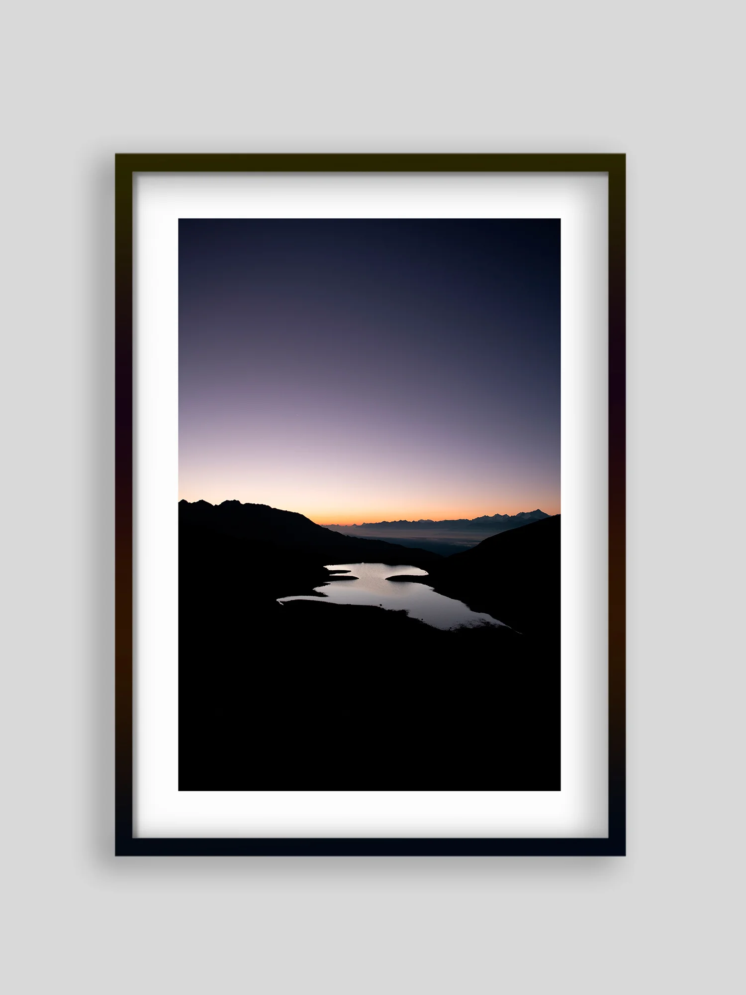 Cadre noir au mur gris présentant une photographie de lac de montagne au crépuscule