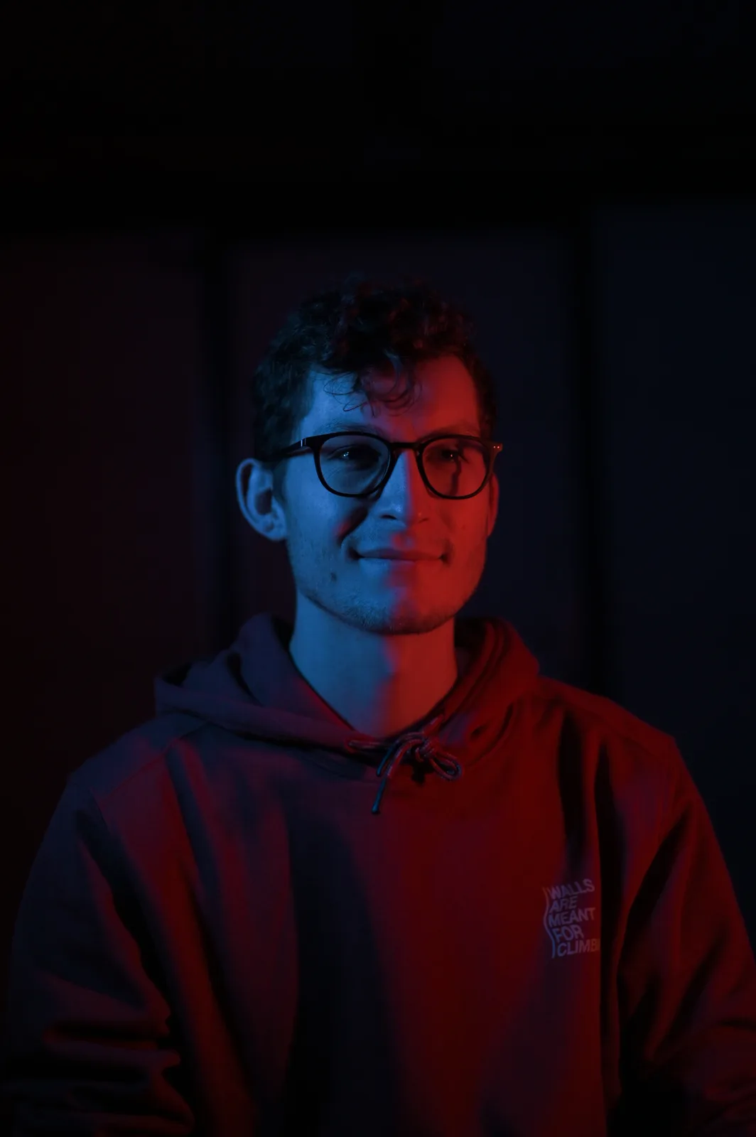 Portrait d'un homme à lunettes en sweat à capuche, éclairé en rouge et bleu